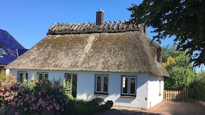 A traditional thatched-roof cottage with white walls, a brick pathway, and pink flowering bushes. - Farsighted Modern Retreat (Taarstedt)