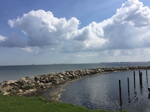 A coastal scene with a rocky breakwater, calm water, and a distant shoreline.