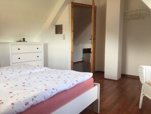 Een slaapkamer met een bed, een witte kapstok, een houten deur en een rieten stoel.