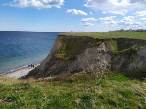 Une falaise côtière, avec un sommet recouvert d’herbe et une plage à sa base.