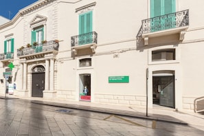 A building with a black door, a green sign reading "UNITED COLORS OF BENETTON", and a "RENTAL SALE 50" sign. - 3906 Corte Degli Aranci by Barbarhouse (Fasano)