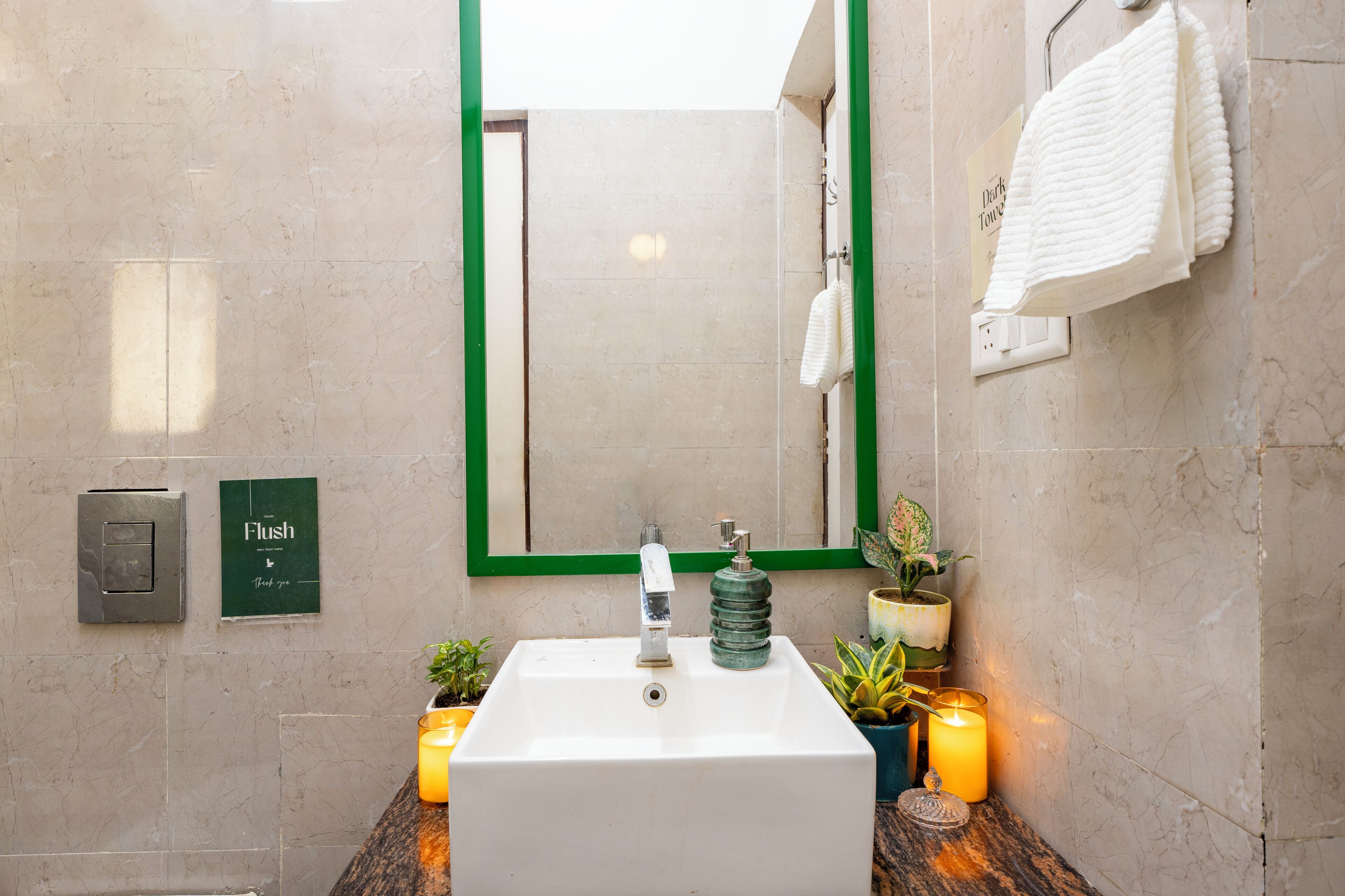 Un baño con lavamanos blanco, espejo con marco verde y una toalla colgada en la pared.