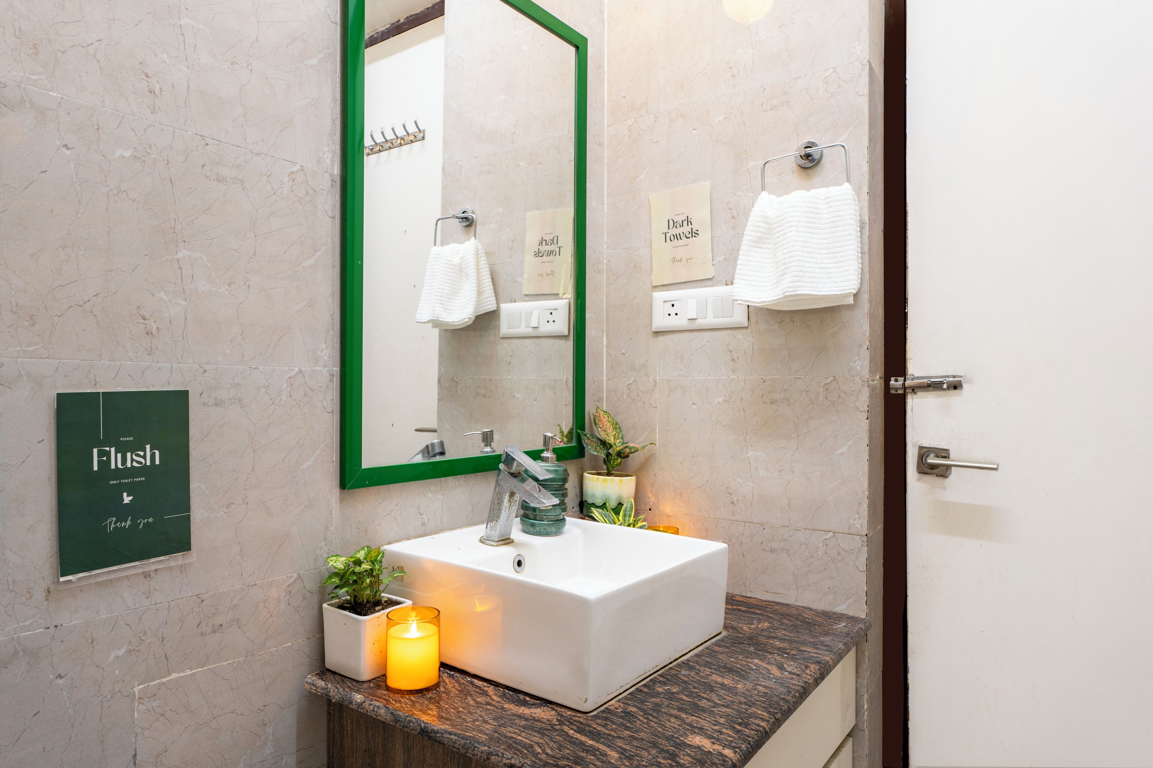 A bathroom with a white sink, green-framed mirror, and a sign that says "Flush".