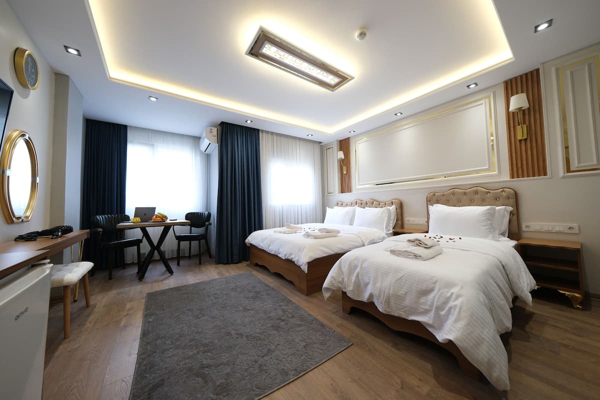 A modern hotel room with two beds, a desk, and a dining area.