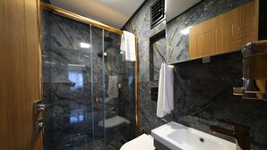 A modern bathroom with a glass-enclosed shower, a white toilet, and a sink with a gold faucet. - Elita Otel (Istanbul)