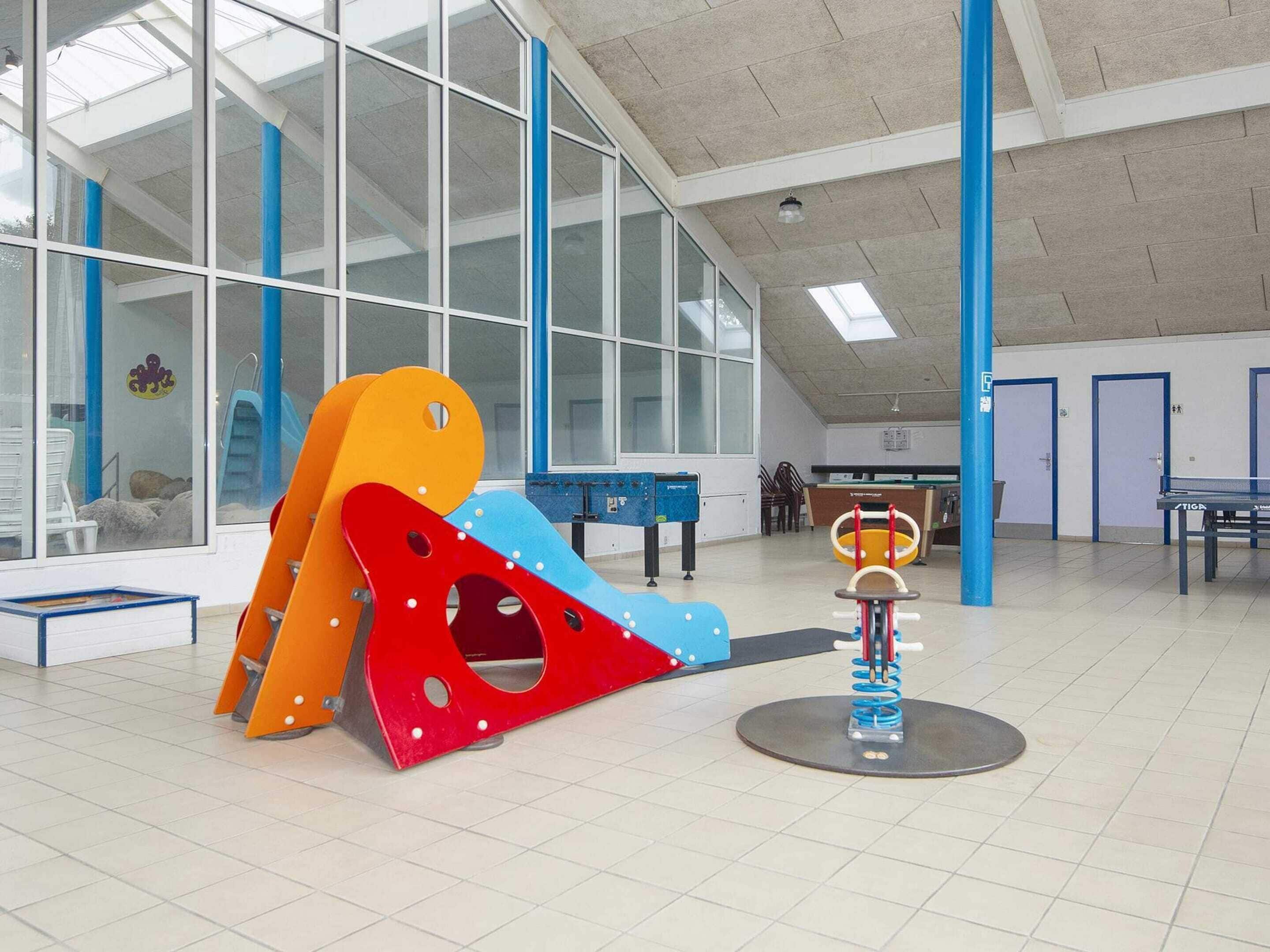 Ein geräumiger Indoor-Spielbereich mit Klettergerüst, Tischtennisplatte und einer kleinen Sitzecke.