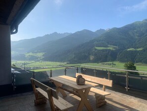 A wooden table and benches on a balcony with a mountain view. - Apartment Uttendorf Near Ski Lift (Uttendorf)