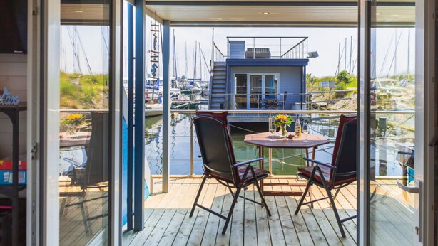 An open deck with a table and chairs, overlooking a marina with boats and a houseboat. - ISA Comfortable Holiday Residence (Grossenbrode)
