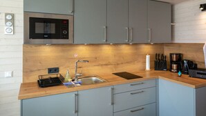A modern kitchen with grey cabinets, a stainless steel sink, a microwave, and various appliances. - ISA Comfortable Holiday Residence (Grossenbrode)