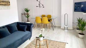 A modern living room with a blue sofa, yellow chairs, a glass dining table, and a TV on the wall. - NEW Gorgeous Central Apartment - Beachfront - 3 BD (SAN SEBASTIAN)