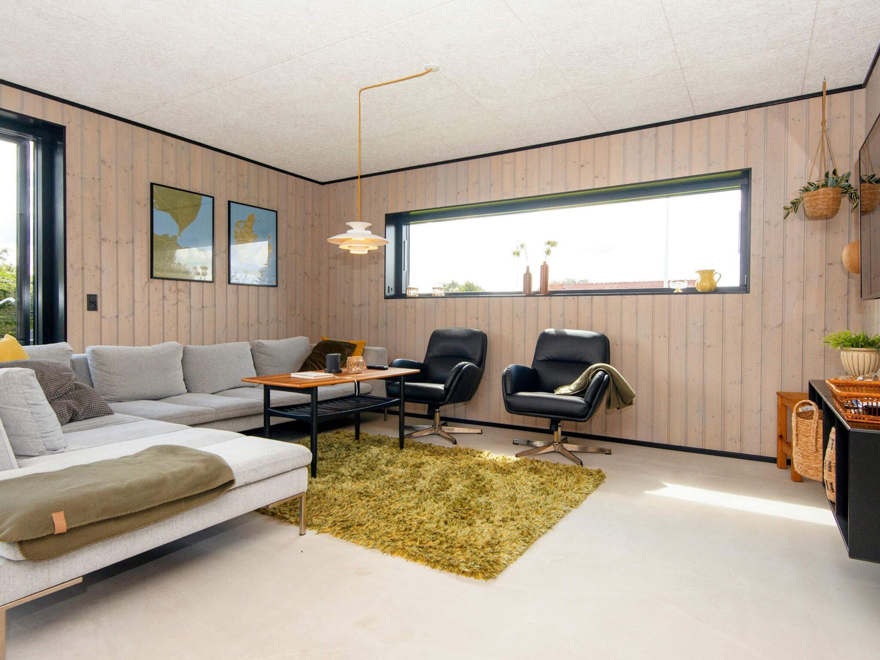 Un salon moderne avec un canapé, deux fauteuils, une table basse et une grande fenêtre.