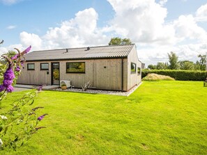 A modern house with a sloped roof, a wooden exterior, and a well-maintained lawn. - 8 Person Holiday Home in Hejls (Hejls)