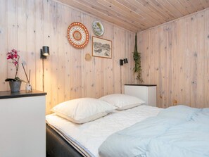 A bedroom with a wooden wall, a bed with white bedding, a small table with a potted plant, and wall-mounted decor. - 8 Person Holiday Home in Hejls (Hejls)