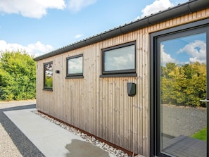 Un bâtiment moderne en bois, doté de grandes fenêtres et d’une porte, entouré de gravier et de verdure.