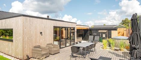 A wooden deck with outdoor seating, a grill, and a building with a sign reading 'FRIHEDEN'.
