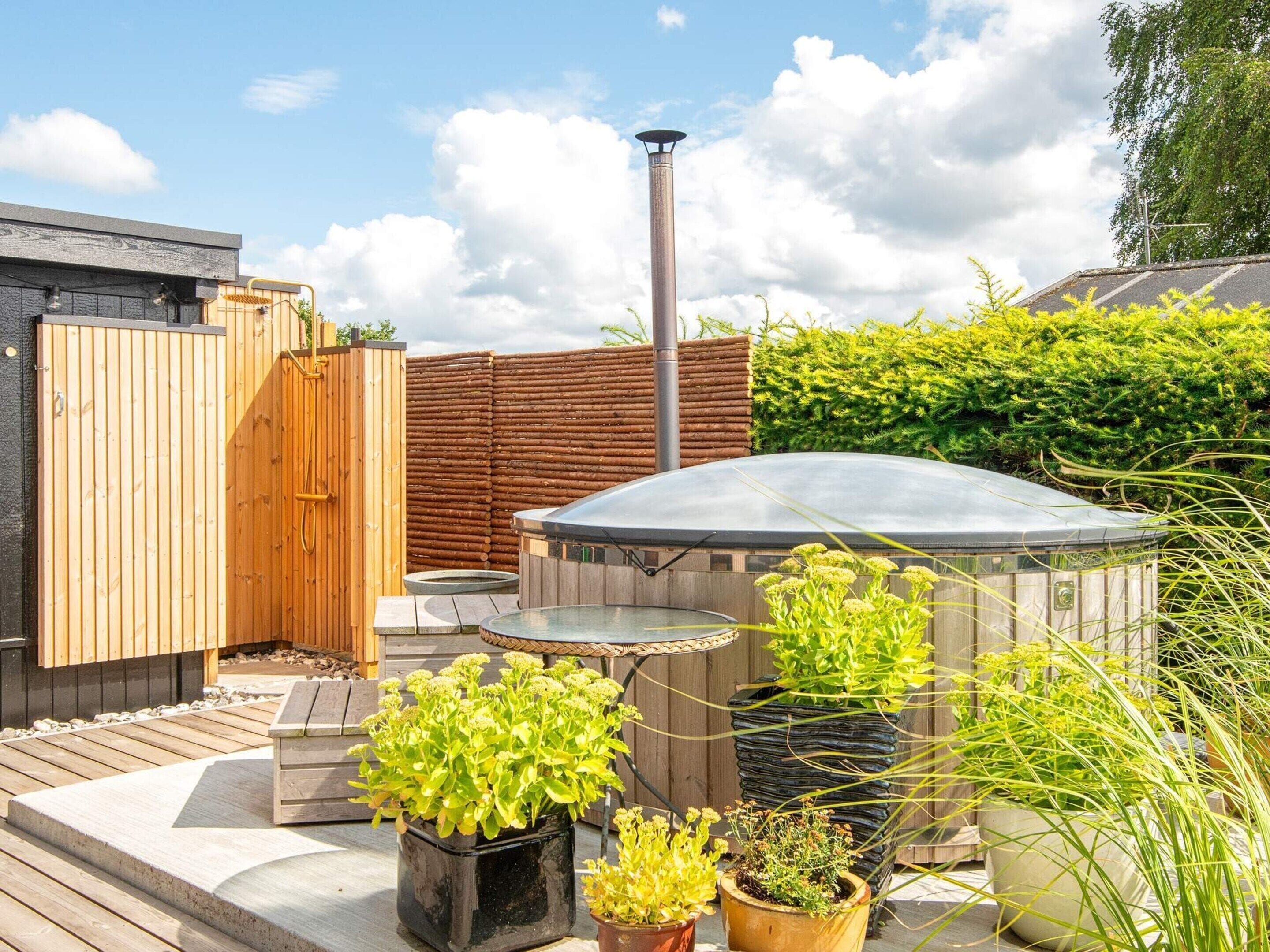 A hot tub, wooden deck, and potted plants in a backyard setting.