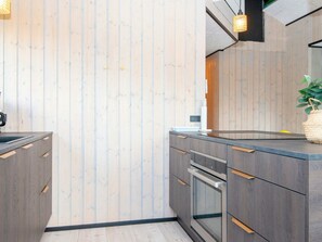 A modern kitchen with wooden panel walls, a built-in oven, and a sink. - 8 Person Holiday Home in Hejls (Hejls)