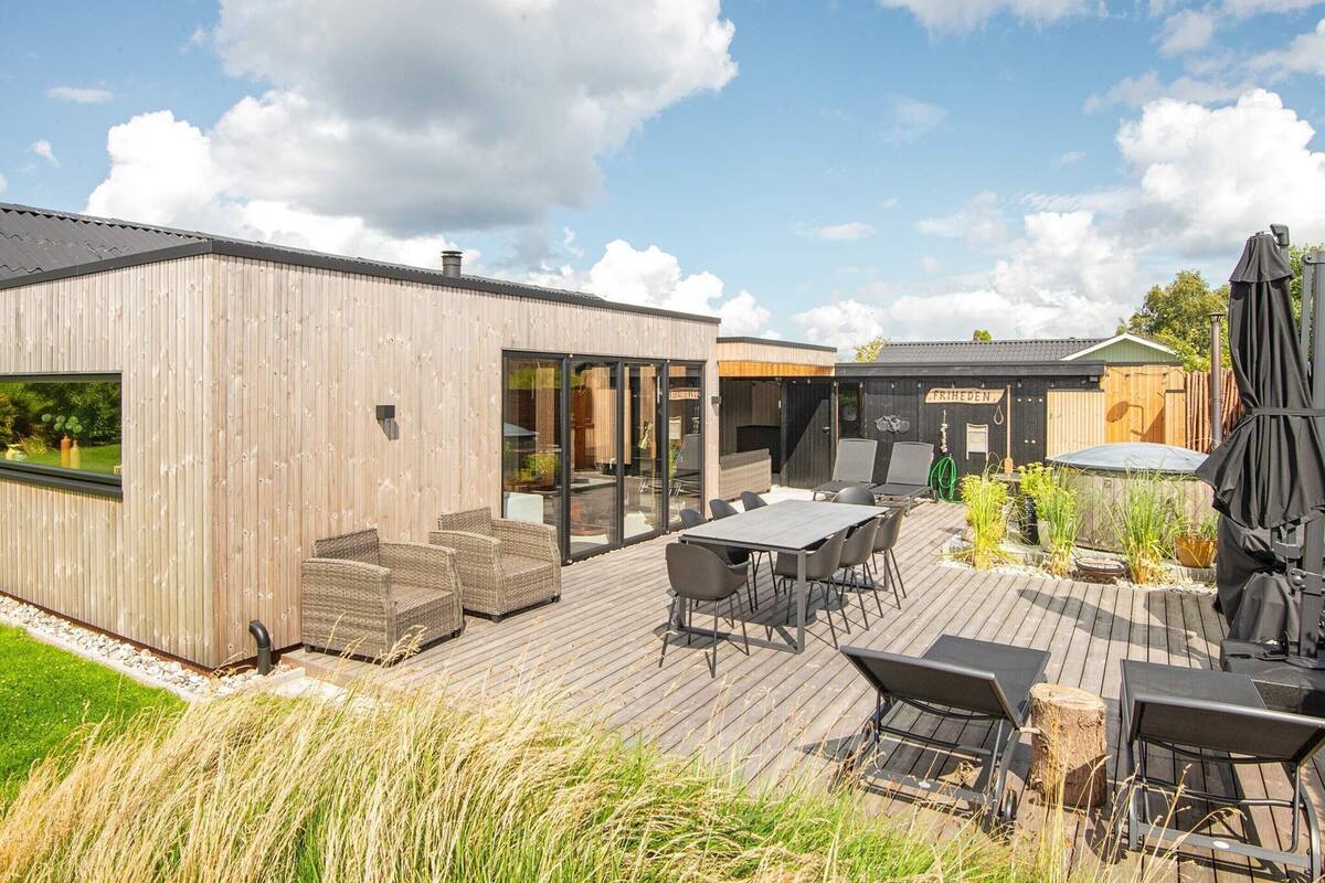 A modern outdoor patio with wooden decking, outdoor seating, and a covered grill area.