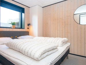 Une chambre à coucher avec un lit, une fenêtre, un miroir fixé au mur et une plante en pot.