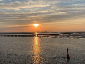 A beach with a sunset, calm water, and a buoy. - Holiday Apartment Nordwind (Wrixum)