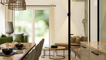 Un comedor moderno con una mesa de madera, sillas y una mesita redonda con un cuenco. Se ve un sofá y una planta al fondo.