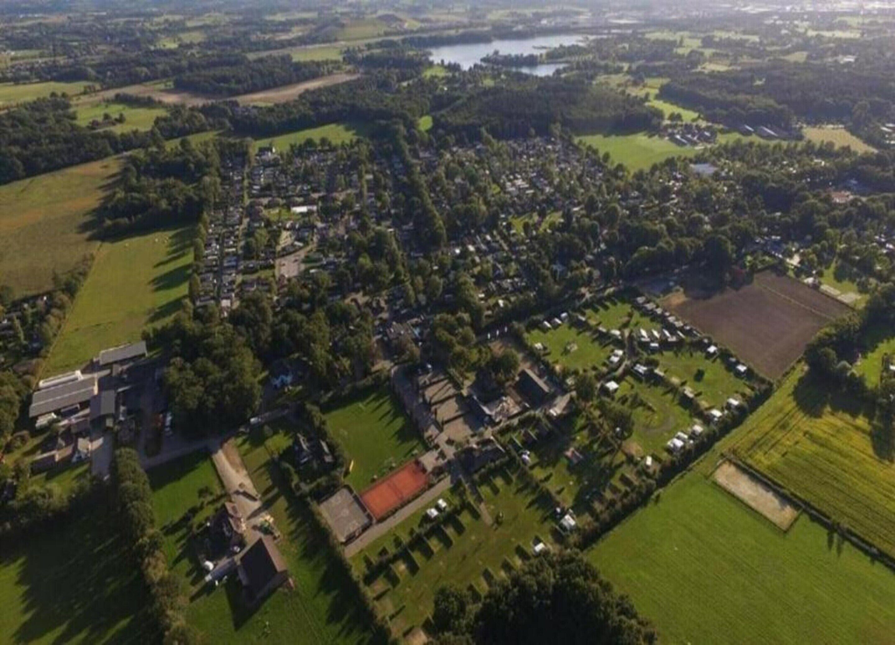 Luchtbeeld van een woongebied met huizen, groenstroken en een groot open veld.