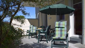An outdoor patio with green chairs and a table, an umbrella, and a small garden area. - Holiday Apartment Seagull (Zinnowitz)