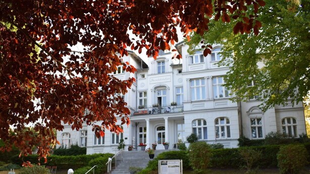 A grand building with a symmetrical facade, multiple windows, and a central entrance with steps leading up to it. - Holiday Apartment Seagull (Zinnowitz)