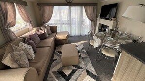 A modern living room with a sofa, ottoman, dining table, chairs, and a TV.