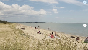 A beach with people relaxing and playing, a clear sky, and a calm sea.