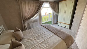 A bedroom with a large bed, beige curtains, a wardrobe, and a view of a balcony.