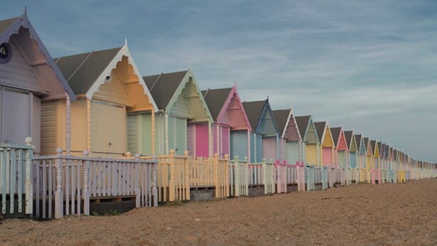 A row of beach huts with a white fence in front, each with a distinct roof style.