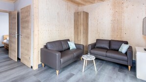 A modern interior with two leather sofas, a small round table, and wooden panel walls. - Familienfreundliche Bungalows am Kronenburger See (Hallschlag)