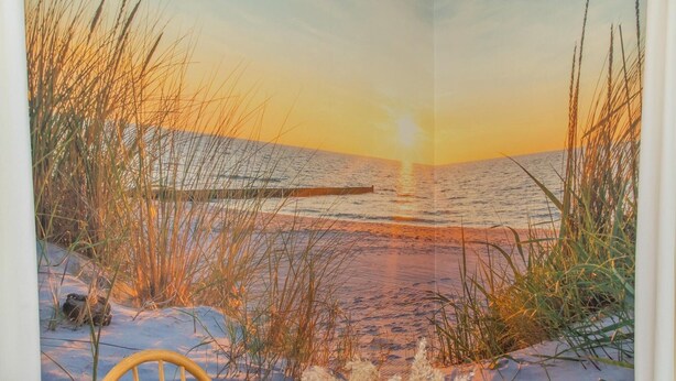 A beach scene with a sunset, a wooden chair, and a table with a vase of dried plants.