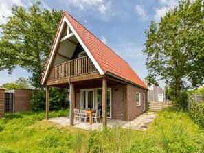 A single-story house with a red roof, a balcony, and a patio with a table and chairs.