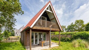 A single-story house with a sloped roof, a balcony, and a patio area with outdoor furniture.
