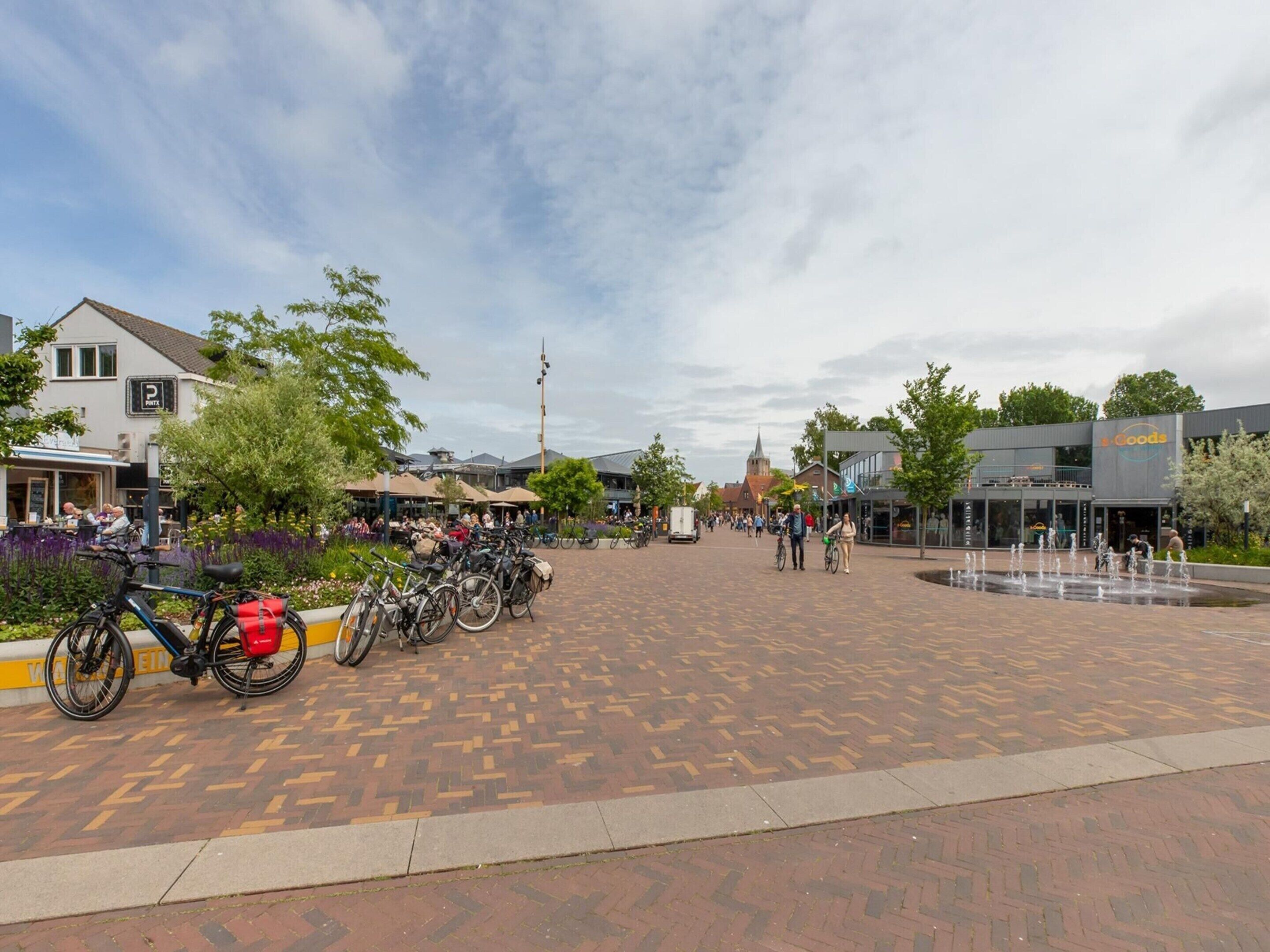Une place publique avec une fontaine, des vélos garés et des bâtiments en arrière-plan.