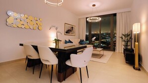 Un salon moderne avec un coin repas, offrant une vue sur la ville grâce à de grandes fenêtres, agrémenté d’un élément décoratif mural et doté d’un éclairage contemporain.