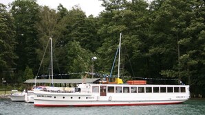 Un grand bateau blanc, orné de bandes rouges et doté d’un pont couvert, était amarré près d’une zone boisée.