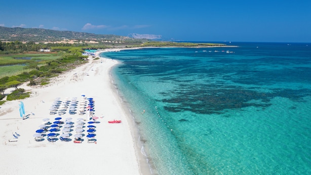 A beach with clear turquoise waters, a white sandy shore, and rows of blue umbrellas. - Hotel Club Cala Fiorita (Budoni)