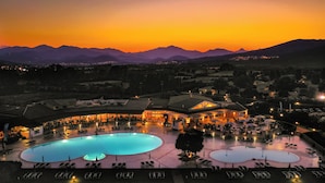 A resort with a large pool, outdoor seating, and a view of mountains. - Hotel Club Cala Fiorita (Budoni)
