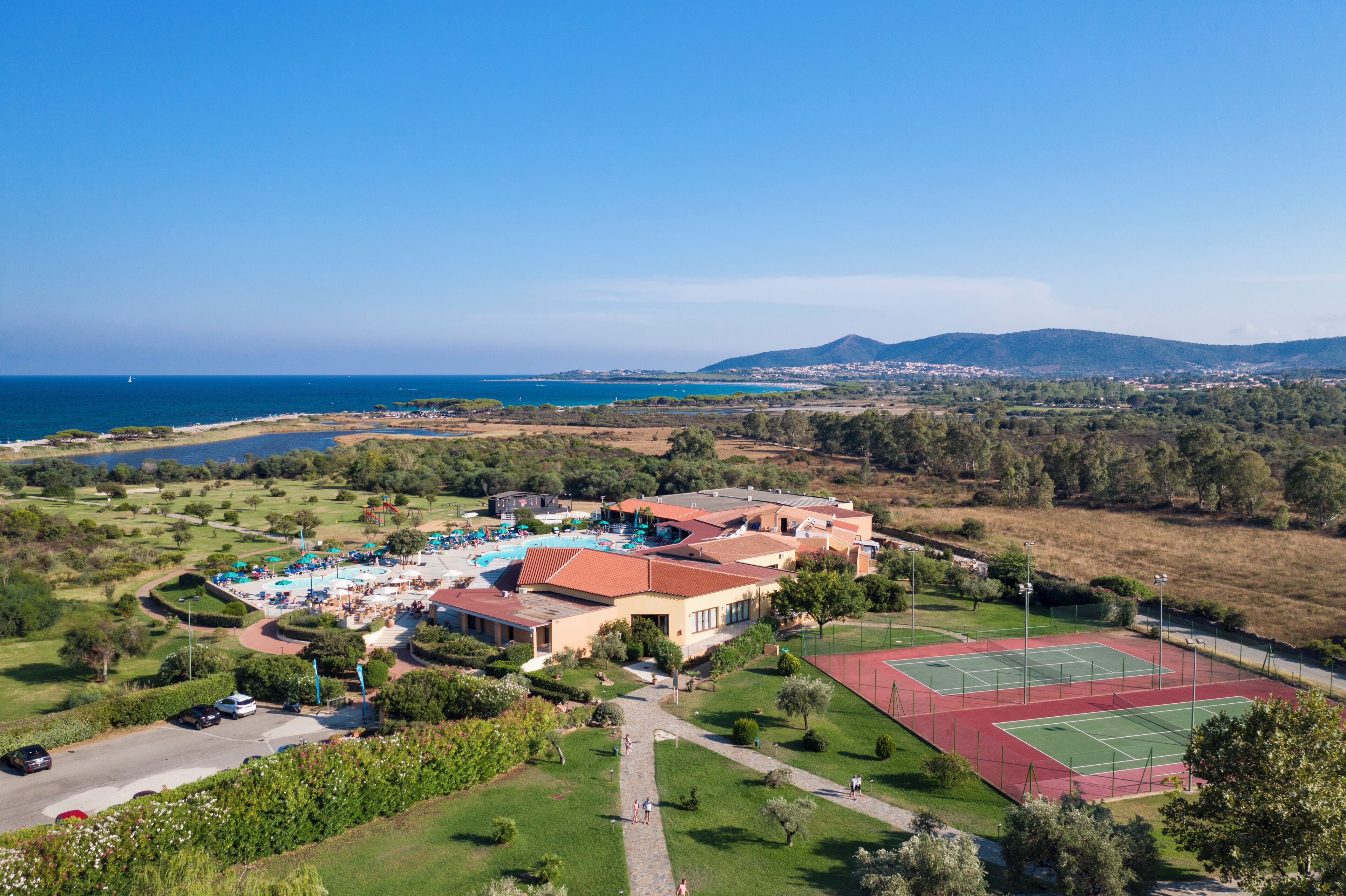 Vista aérea de un resort con piscina, canchas de tenis y vista al mar.