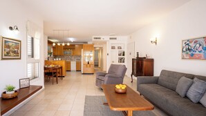 A modern living room with a grey sofa, a wooden coffee table with fruit, a grey armchair, and a dining area with a table and chairs. - Homey Kiryat Haim Apt by Sea N Rent (Haifa)