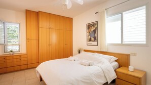 A bedroom with a bed, wooden wardrobe, bedside table, and a window with blinds. - Homey Kiryat Haim Apt by Sea N Rent (Haifa)