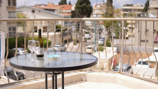 A round table with a bottle of wine and two glasses on a balcony with a metal railing. - Homey Kiryat Haim Apt by Sea N Rent (Haifa)