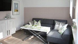 A modern living room with a sofa, a coffee table, and a flat-screen TV mounted on the wall. - Cosy Apartment in Schmogrow (Schmogrow)