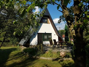A triangular house with a sloped roof, a window, and a door. There is a patio with chairs and a table. - Cosy Apartment in Schmogrow (Schmogrow)