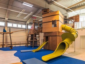 Un espace de jeux intérieur comprenant un toboggan, des structures d’escalade et une cabane de jeux en filet.