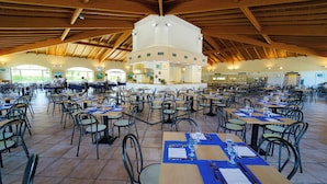 A spacious dining area with multiple tables and chairs, a high ceiling with wooden beams, and a central kitchen area. - Futura Club La Praya (Pizzo)