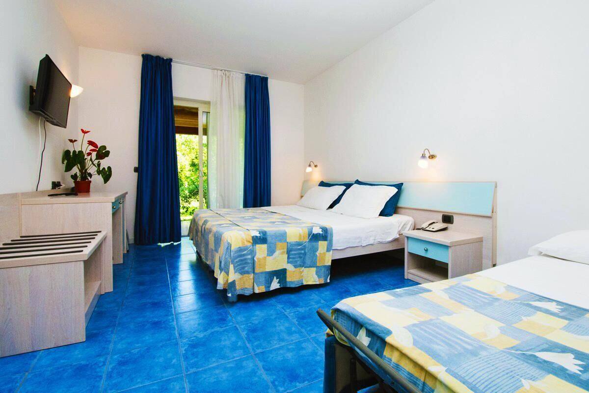A hotel room with a bed, a desk, a chair, a TV, and a window with curtains.